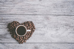 Volle Kaffeetasse auf einem Herz aus Kaffeebohnen auf einem hellen Holztisch